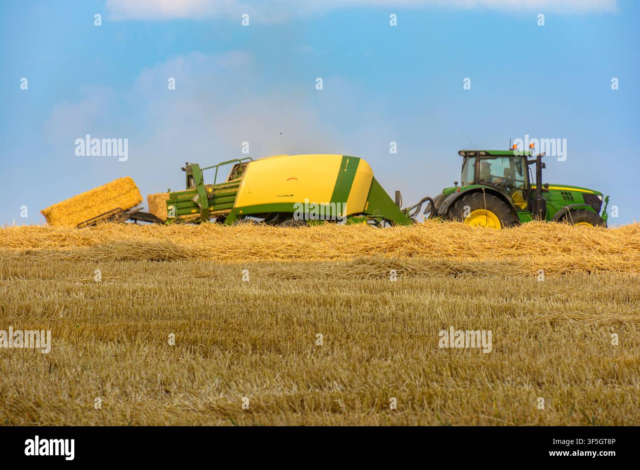 Traktor mit Ballenpresse, der rechteckige Strohballen auf einem Feld in Coesfeld, Deutschland, entlädt - August 2026 Stockfoto