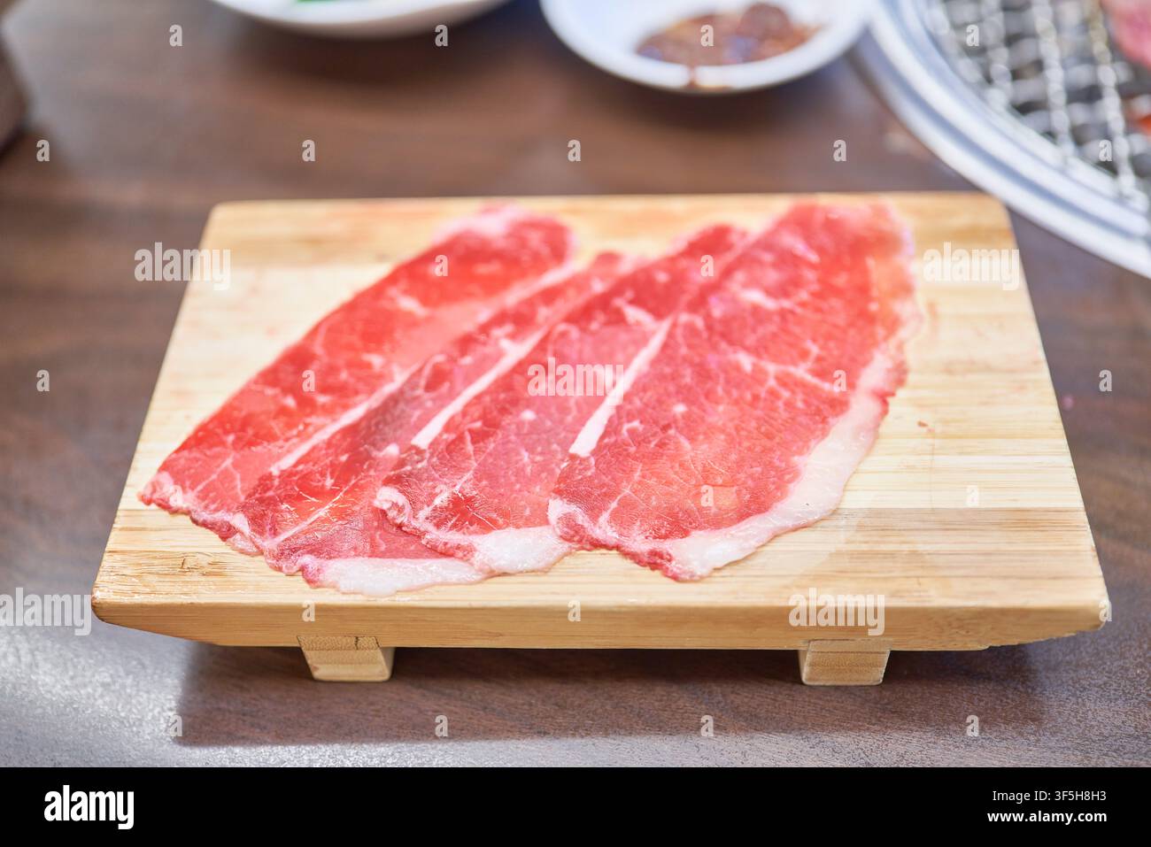 Verschiedene rohe koreanische Fleischstücke auf einem Holzbrett neben einem Holzkohlegrill, zubereitet für ein traditionelles koreanisches Barbecue-Essen. Stockfoto