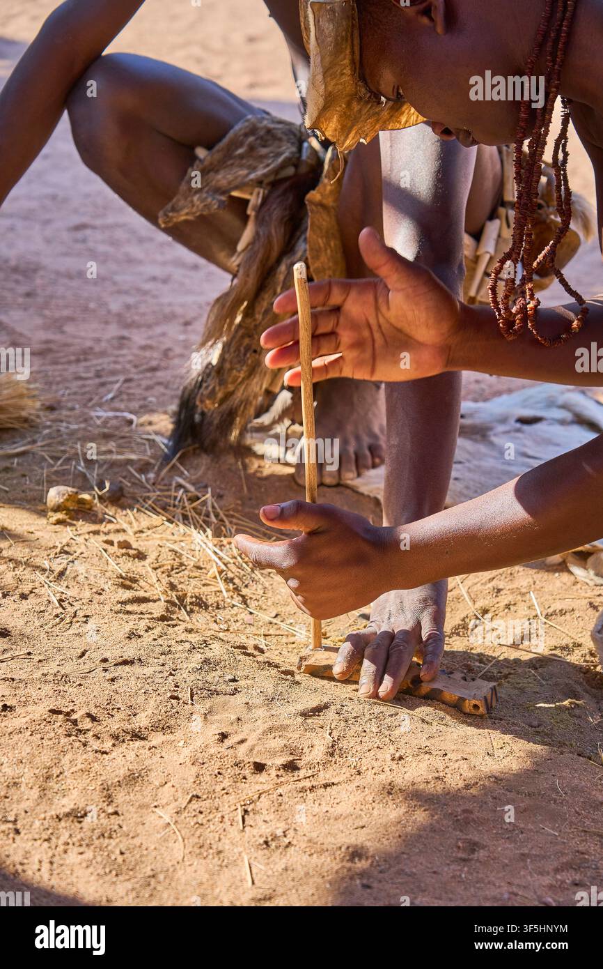 Leichte Rauchspuren beginnen aufzusteigen, während ein junger afrikanischer Stammesmann schnell einen hölzernen Reibrührer gegen ein Grundbrett dreht, um ein Feuer zu entzünden. Stockfoto