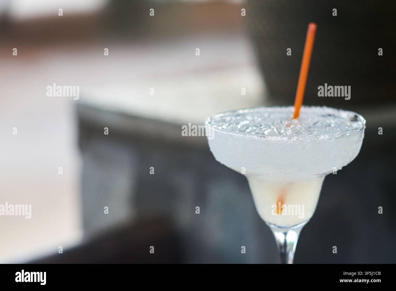Nahaufnahme eines erfrischenden gefrorenen Cocktails, serviert in einem Stielglas mit salziger Rand und einer Orangenstrohhalm. Stockfoto