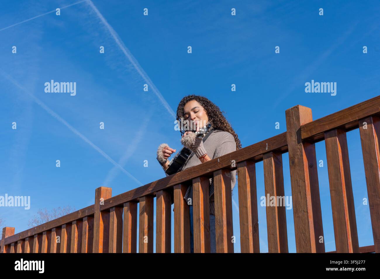 Junge Frau spielt ein Streichinstrument und genießt Musik im Freien an einem sonnigen Tag Stockfoto