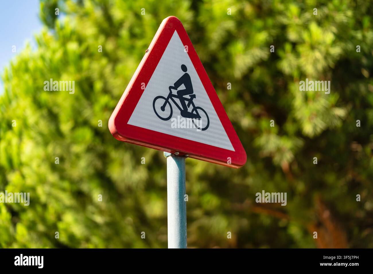 Nahaufnahme eines dreieckigen Fahrradwarnschilds vor verschwommen grünen Bäumen in einer Stadtszene Stockfoto