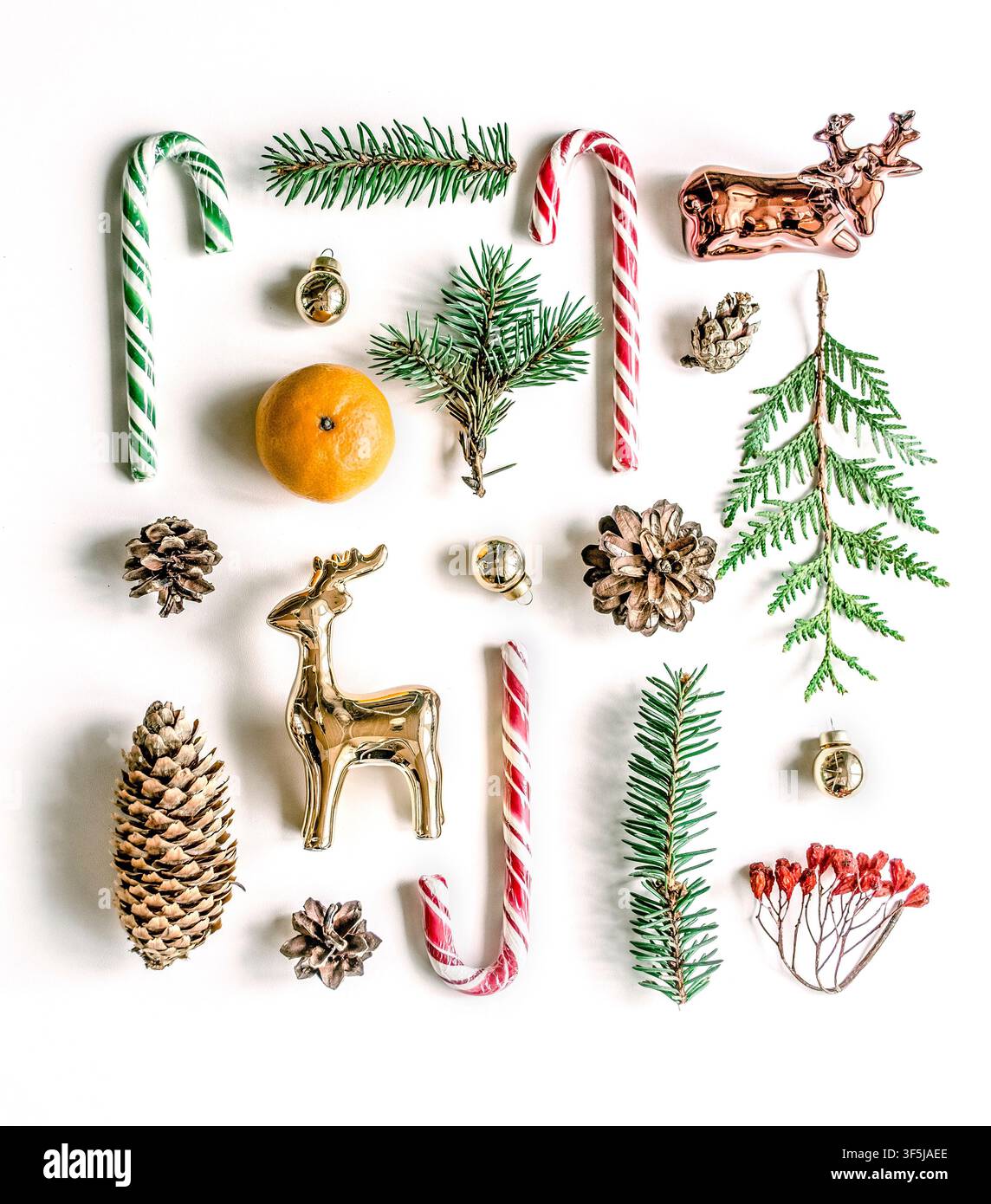 Weihnachts-Flatlay von oben auf weißem Hintergrund mit roten und grünen Zuckerstangen, Tannenzweigen, Tannenzapfen, goldenen Rentierornamenten, Kugeln und hellbraunem Hintergrund Stockfoto
