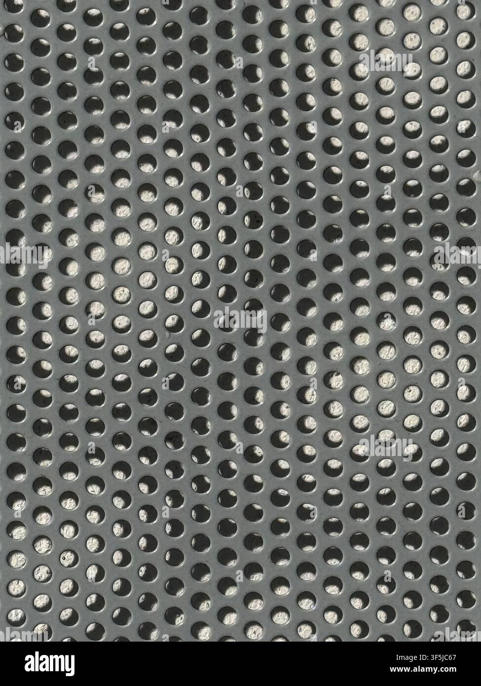 Abstrakte Nahaufnahme-Textur eines grauen perforierten Metallblechs mit einem geordneten Raster kreisförmiger Löcher, metallischen Reflexionen, Schatten und einer Industrie Stockfoto