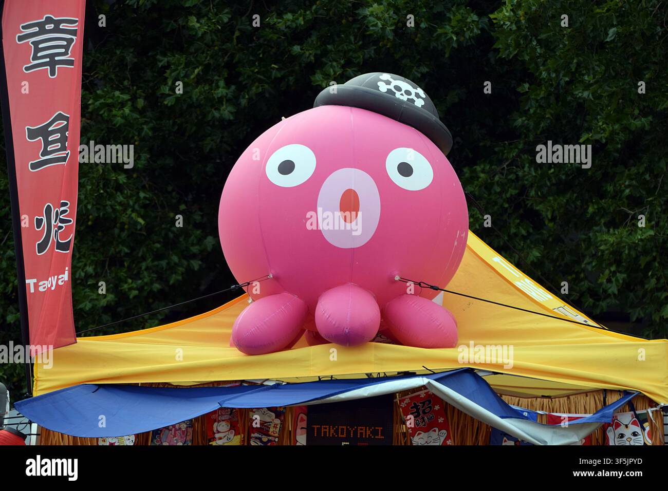 Riesige rosa Tintenfisch-Maskottchen über einem Takoyaki-Japanisch-Straßenimbiss auf einem Sommerfest Stockfoto