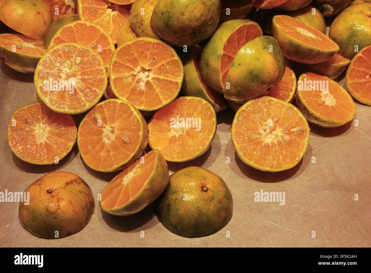 Halbierte thailändische Sai Nam Phueng-Mandarinens zeigen saftiges orangefarbenes Fruchtfleisch und grüne Schalen, präsentiert als frische Zitrusfrüchte zur Saftgewinnung. Stockfoto