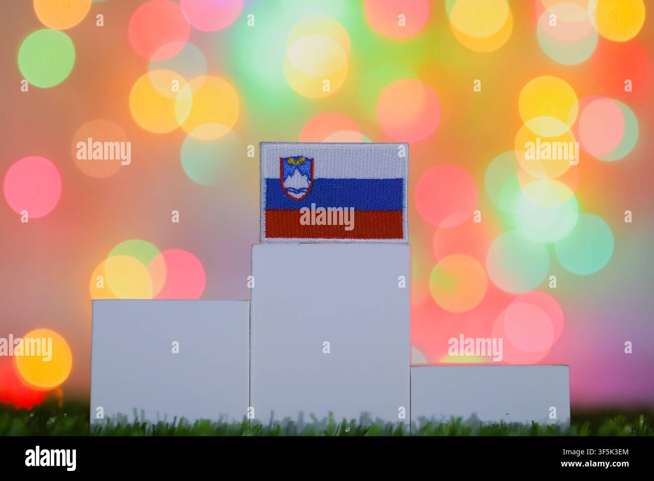Die Nationalflagge Sloweniens, die auf dem höchsten Podest vor farbenfrohem Bokeh gezeigt wird, repräsentiert den ersten Platz, nationalen Stolz und Sieg. Stockfoto