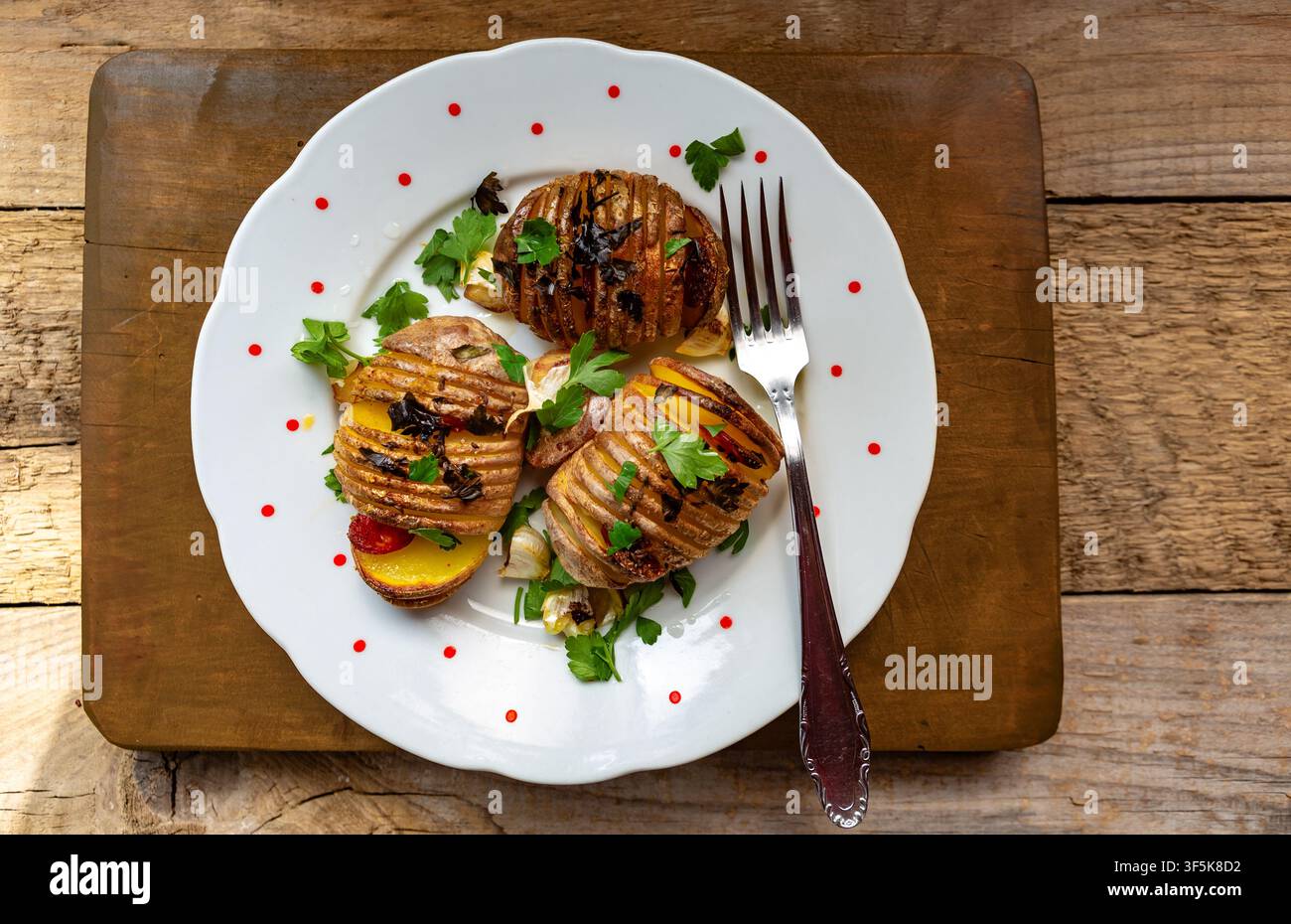 Knusprige, goldene hausgemachte Hasselback-Kartoffeln, perfekt geröstet mit duftenden frischen Kräutern, ganzen Knoblauchzehen und einem reichhaltigen Tropfen extra nativem Olivenöl Stockfoto