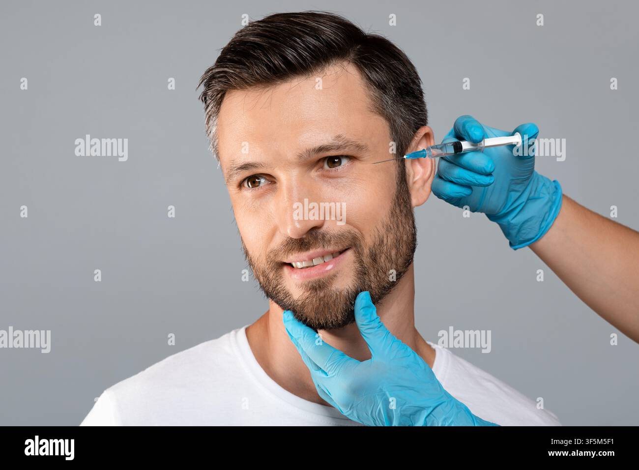 Hübscher Mann, der unter Augeninjektionen kommt, grauer Hintergrund, leerer Raum Stockfoto