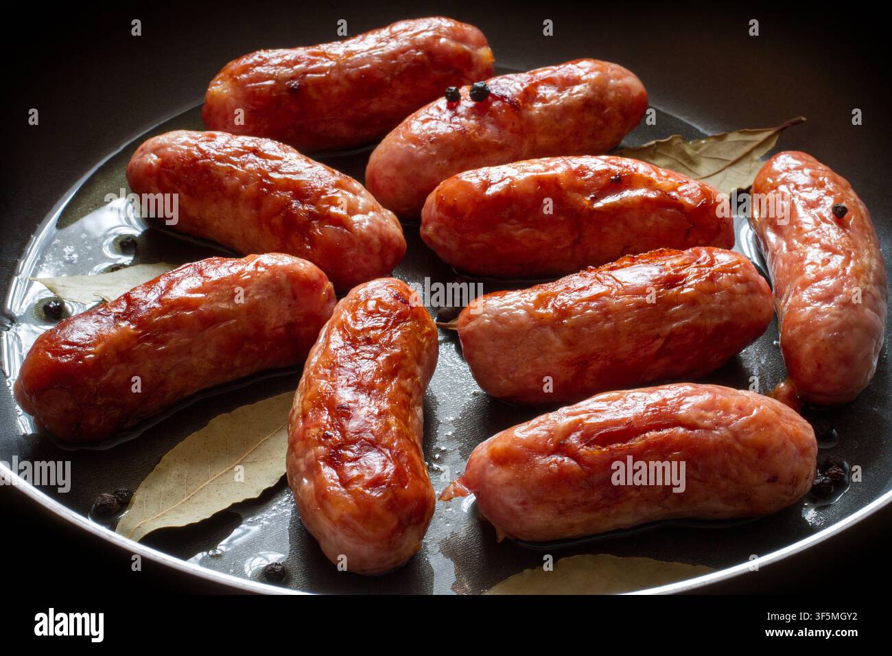Gebratene Fleischwurst in einer Pfanne, Nahaufnahme. Frische Würste mit Paprika und Lorbeerblättern. Stockfoto