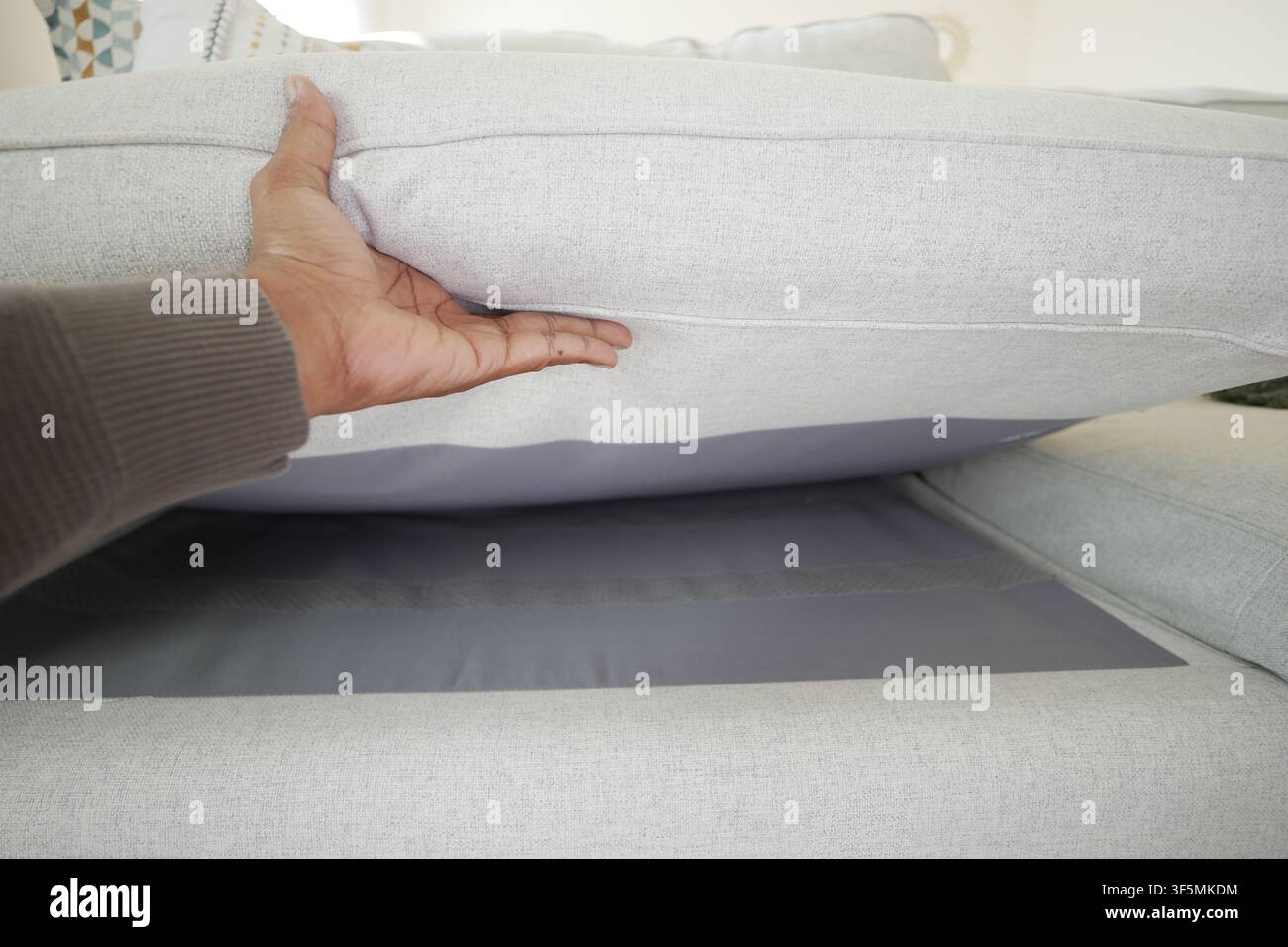 Person, die ein Sofakissen anhebt, um Stauraum freizulegen Stockfoto