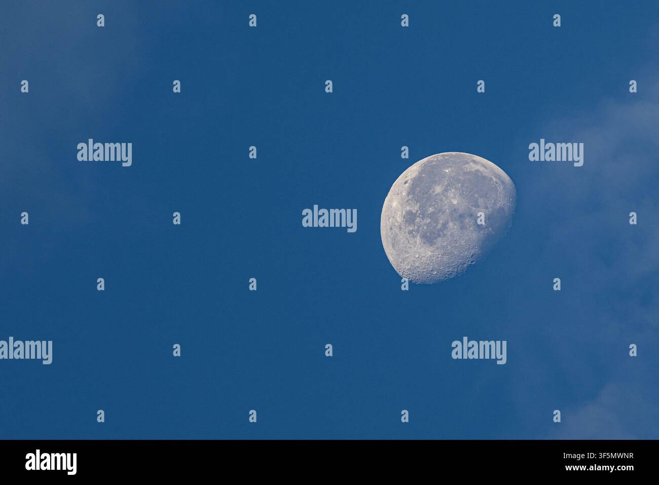 Wachsender Mond im Abnehmenden sichtbar an einem klaren blauen Taghimmel mit sanften Wolken. Stockfoto