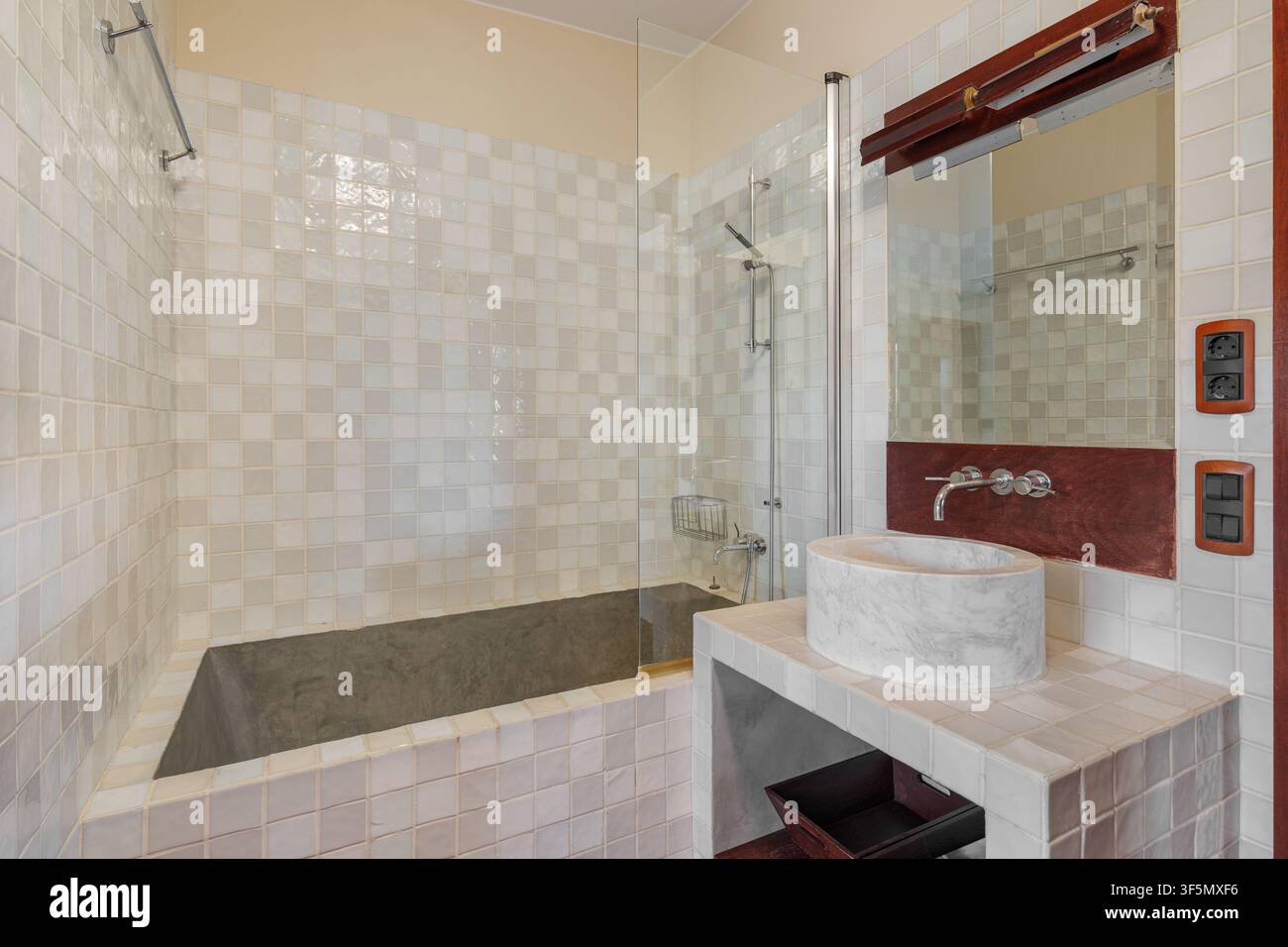 Zeitgenössisches Badezimmerinterieur mit großer eingebauter Badewanne, gefliestem Umfeld, modernem Waschtischspiegel, Arbeitsplattenspüle, neutralen Tönen, hell Stockfoto