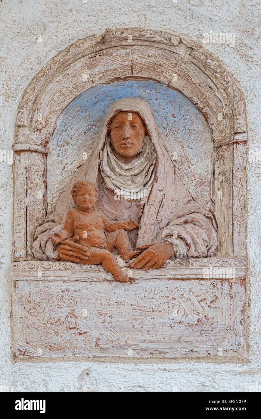 Farbenfrohes Terrakotta-Votivrelief einer Madonna und eines Kindes, das in eine Wandnische einer Straße eingelassen ist, ein traditioneller Straßenschrein. Monopoli, Provinz Bari, Apulien Stockfoto