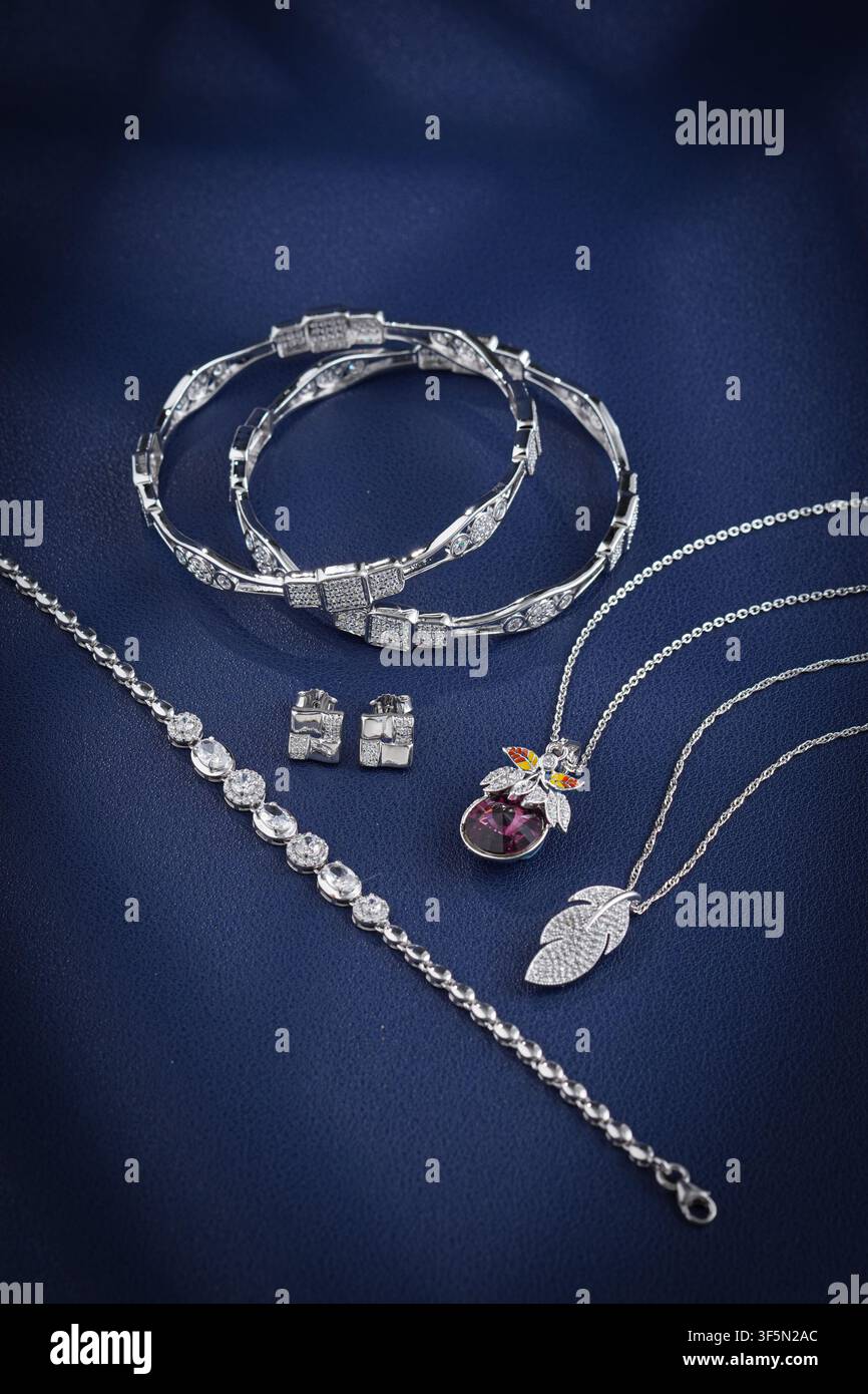 Luxuriöses Sterlingsilber-Schmuckset mit Armbändern, Halsketten, Ohrringen und Edelsteinanhänger, präsentiert auf einem eleganten dunkelblauen Stoffhintergrund Stockfoto