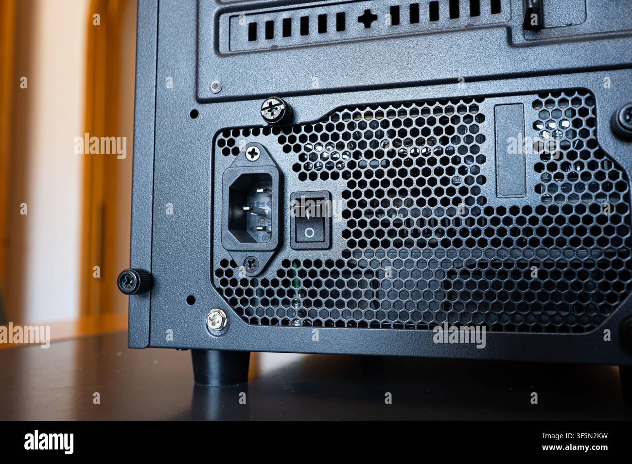 Nahaufnahme der Rückseite eines Desktop-Computergehäuses, das das Netzteil mit Stromanschluss, Kippschalter und Mesh-Ventilation zeigt. Stockfoto