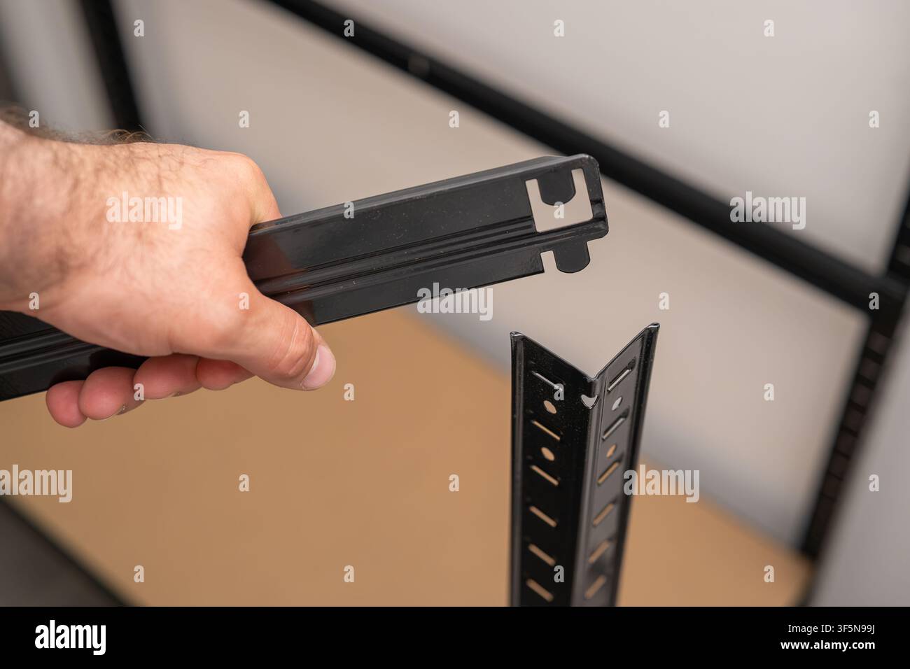 Befestigung einer schwarzen Metallhalterung an der vertikalen Stützschiene eines Regalsystems während des Montagevorgangs. Stockfoto