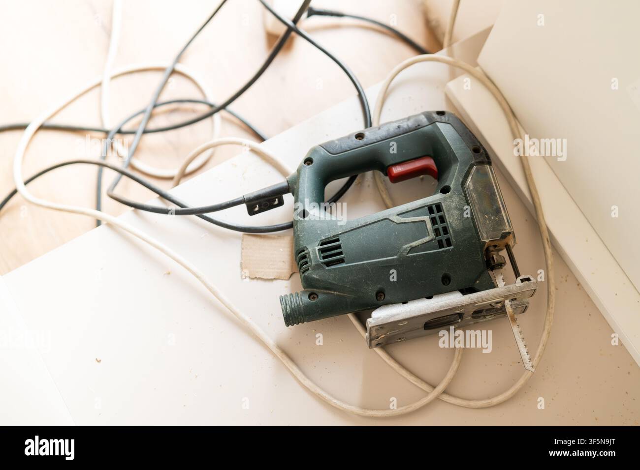 Mit einem Stichsägenwerkzeug Holzmaterialien an einem Heimwerkerarbeitsplatz schneiden. Verhedderte Elektrokabel und Holzspäne sind auf der Arbeitsfläche sichtbar. Stockfoto