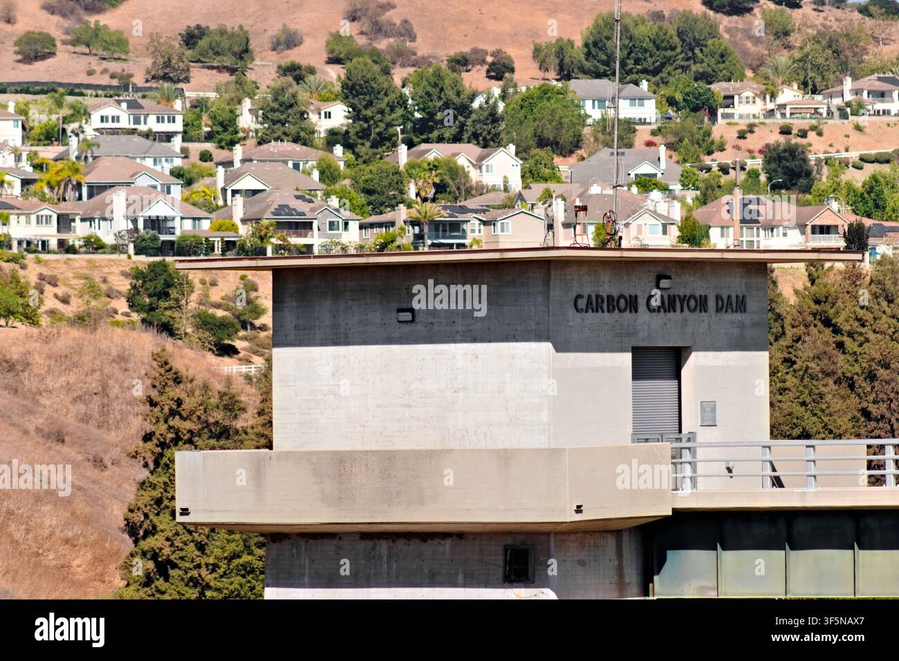 Der Kontrollturm und die Zugangsbrücke des Carbon Canyon Dam stehen unterhalb eines dichten Hügelviertels in den trockenen Ausläufern von Yorba Linda. Stockfoto