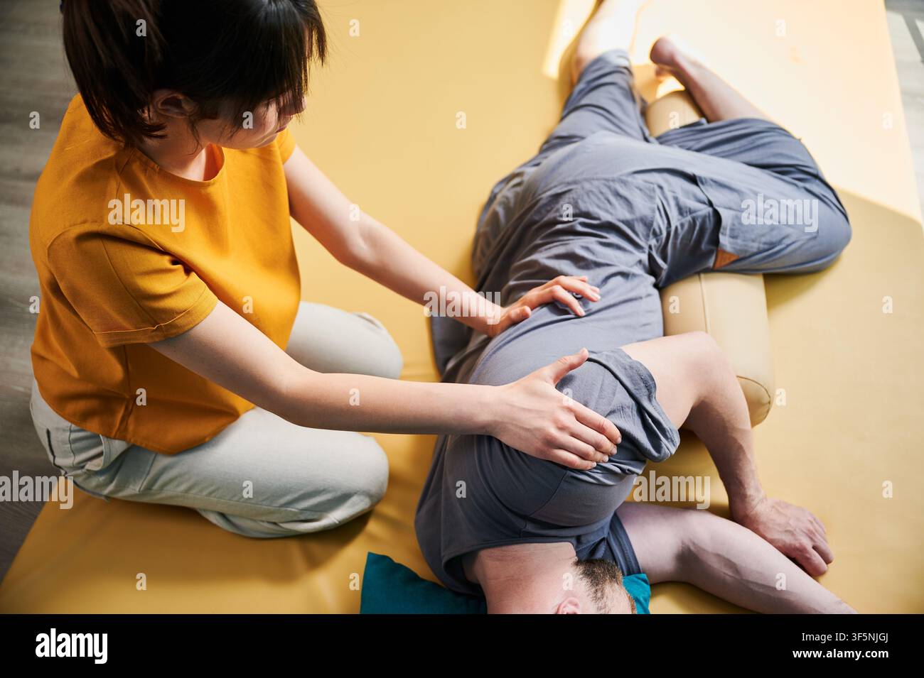 Masseurin, die thai-Yoga-Massage macht. Frau Therapeutin, die traditionelle Massagebehandlung für männlichen Patienten in Innenräumen durchführt. Der Kunde liegt auf der Matte, meditiert und genießt eine Handmassage in ruhiger Atmosphäre. Stockfoto