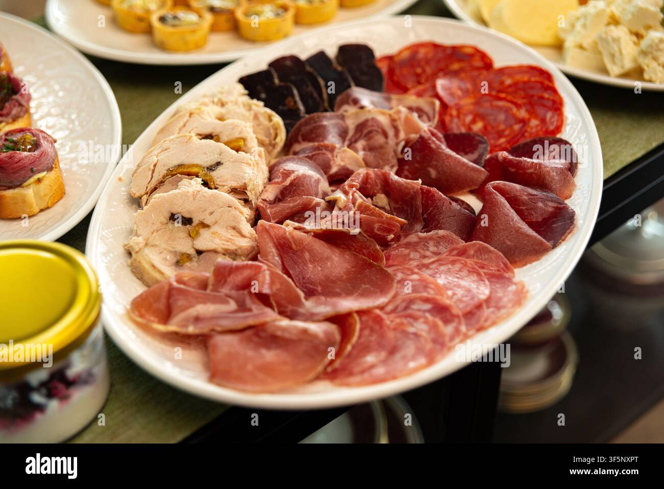 Ein großes weißes Tablett zeigt eine Auswahl an Charcuterie, darunter verschiedene Arten von dünn geschnittenen Schinkensorten wie Prosciutto, Salami und Chorizo Stockfoto