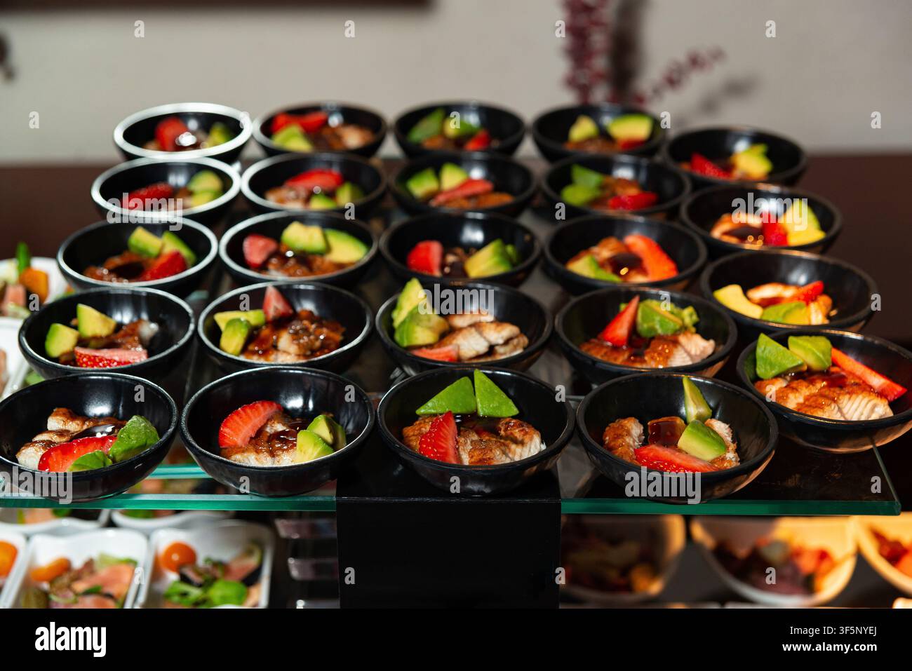 Eine Ausstellung mehrerer kleiner schwarzer Schüsseln, jede gefüllt mit einer bunten Kombination aus Erdbeeren, Avocado und verschiedenen Dessertzutaten. Die Schüsseln Stockfoto
