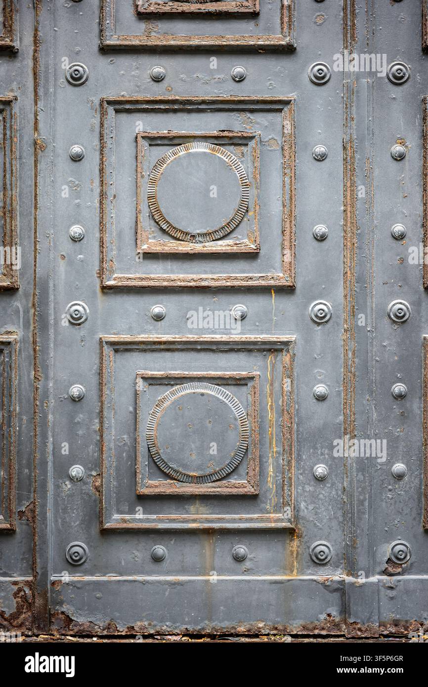 Eine alte rostige Metalltür mit geometrischen dekorativen Formen, Nieten und einer verwitterten Eisenoberflächentextur. Stockfoto