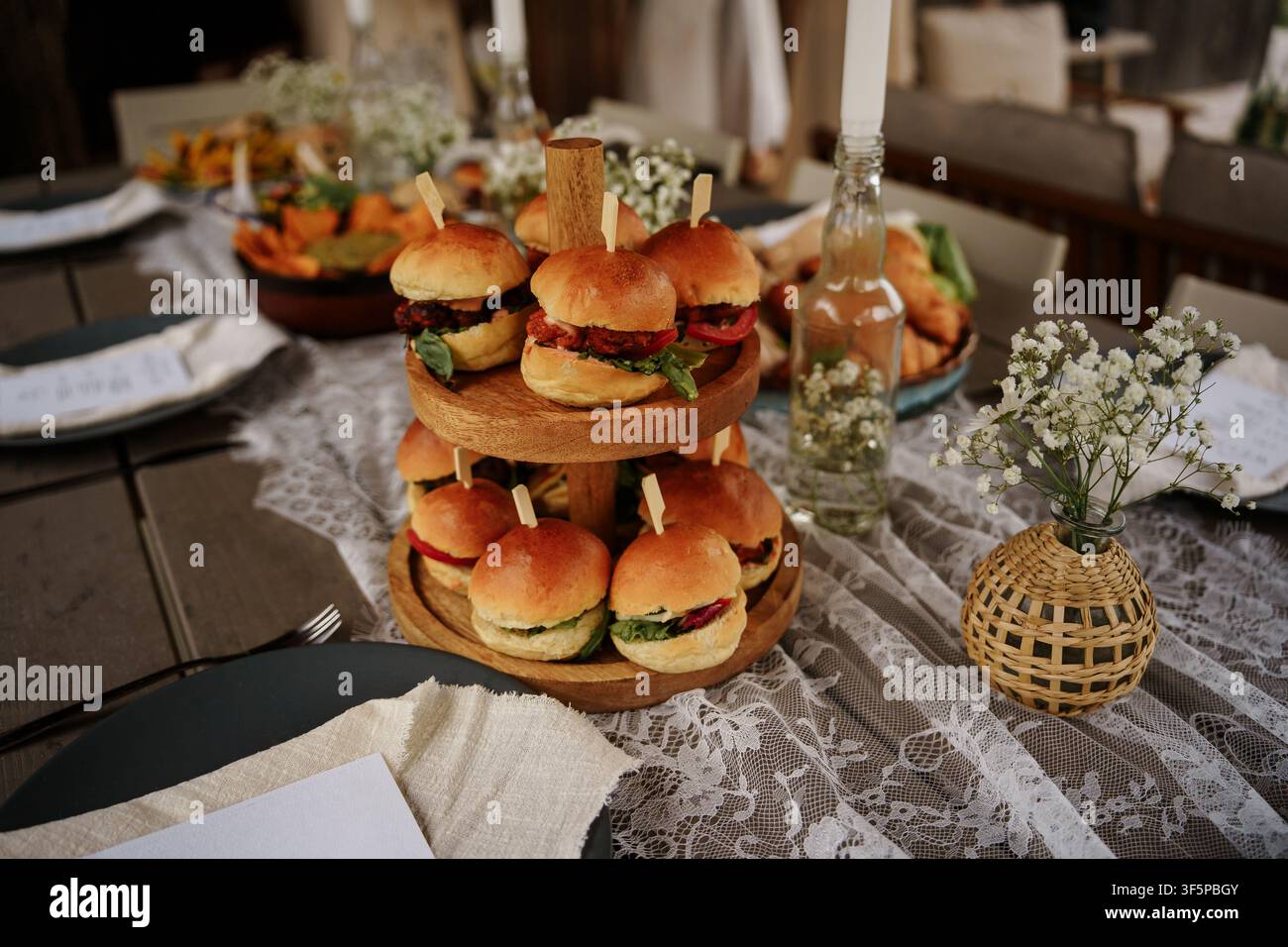 Miniatur-Burger auf einem gestuften Holzservierständer bei einem rustikalen Hochzeitsbankett mit Spitzen-Dekor, Vorspeisen-Catering-Display Stockfoto