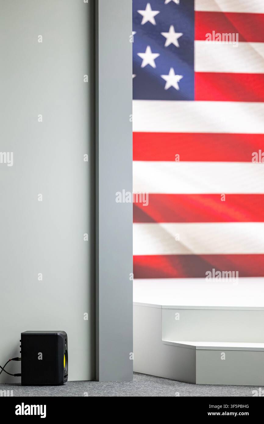 Amerikanische Flagge hinter einer modernen Bühnenplattform mit einem Audiolautsprecher auf dem Teppichboden in einer Inneneinrichtung mit schlichten Wänden und sim Stockfoto