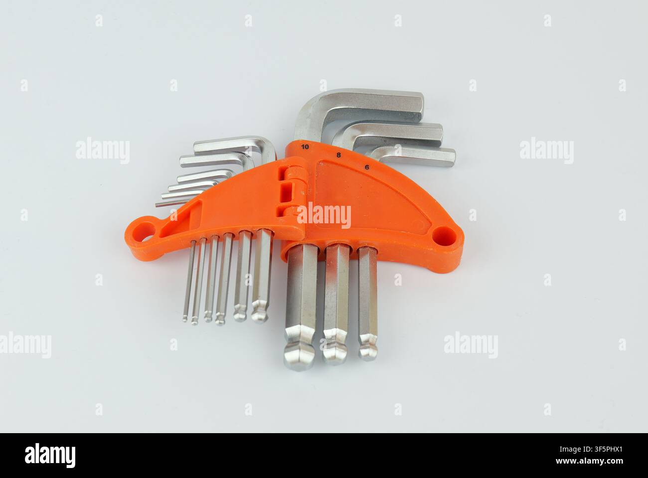 Satz von Metall-Inbusschlüsseln in verschiedenen Größen, die in einem hellen orangefarbenen Kunststoffhalter auf einem hellen Hintergrund angeordnet sind Stockfoto