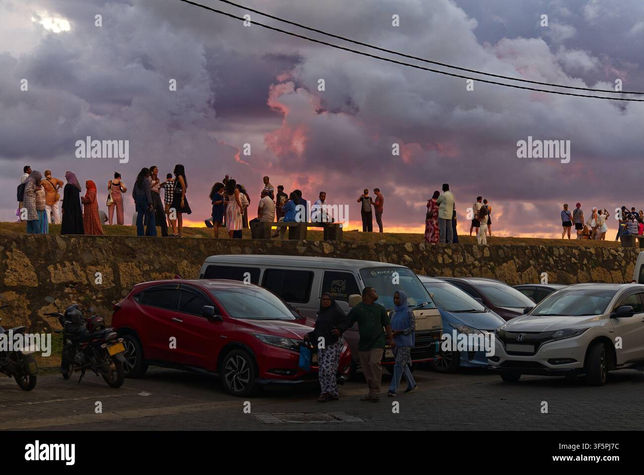 Galle Fort, Sri Lanka – Menschen stehen auf dem Wall in der Rampart Street und beobachten den Sonnenuntergang über dem Indischen Ozean, mit geparkten Autos im Vordergrund Stockfoto