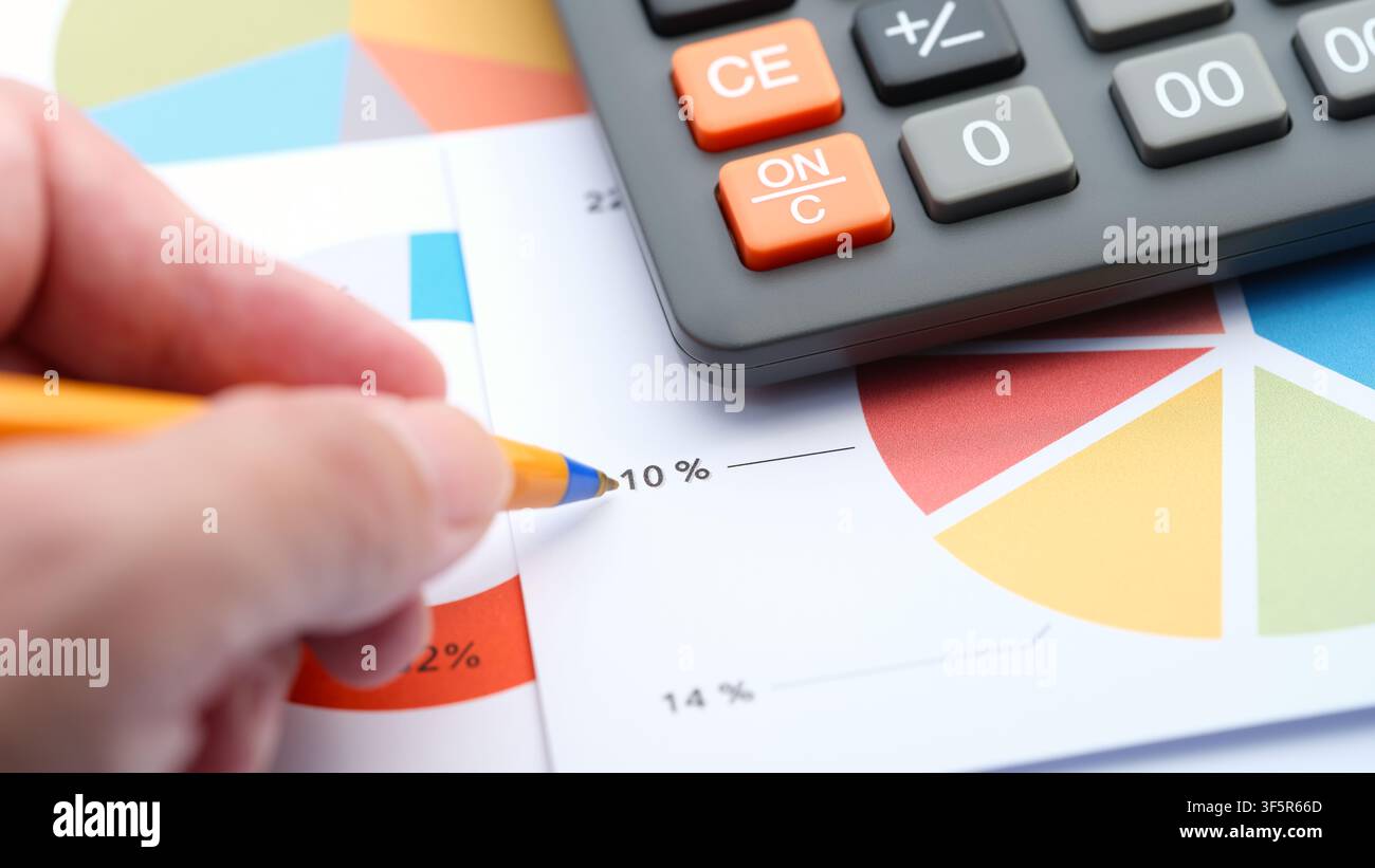 Eine Nahaufnahme einer Hand mit einem Kugelschreiber, der auf ein Finanzdiagramm zeigt, mit einem Taschenrechner in der Nähe. Stockfoto