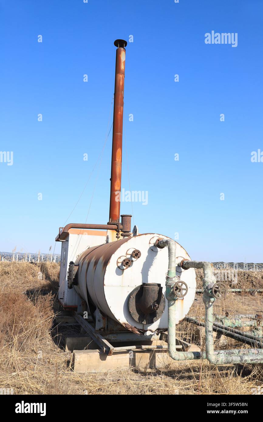 Ein alter horizontaler Industriekessel steht in der Wildnis, gepaart mit einem hohen rostigen roten Schornstein. Rohre und Ventile sind voller Spuren der Zeit. Noch einmal Stockfoto