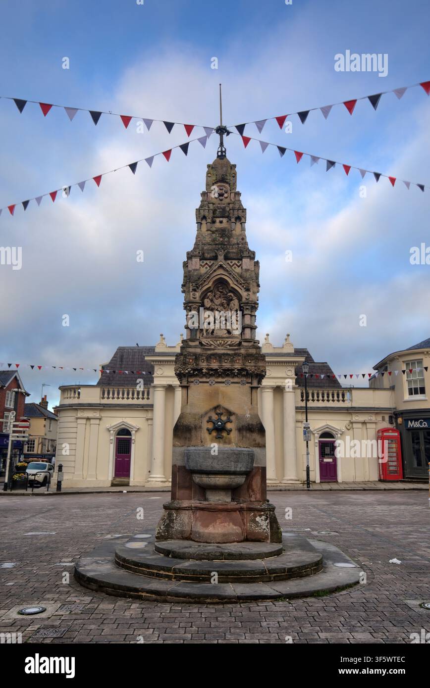 Der Trinkbrunnen im viktorianisch-gotischen Stil mit kunstvollen Bibelszenen, der auf dem Marktplatz unter festlicher Fahnenbehängung in Saffron Walden steht. Stockfoto