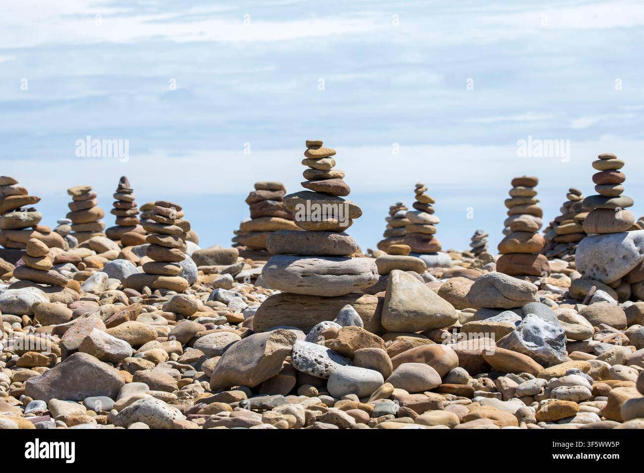 Zahlreiche Steinhaufen und Fels­türme, die über einen Kiesstrand an der Küste von Northumberland unter einem hellen bewölkten Himmel balancieren, Alnmouth, UK. Stockfoto