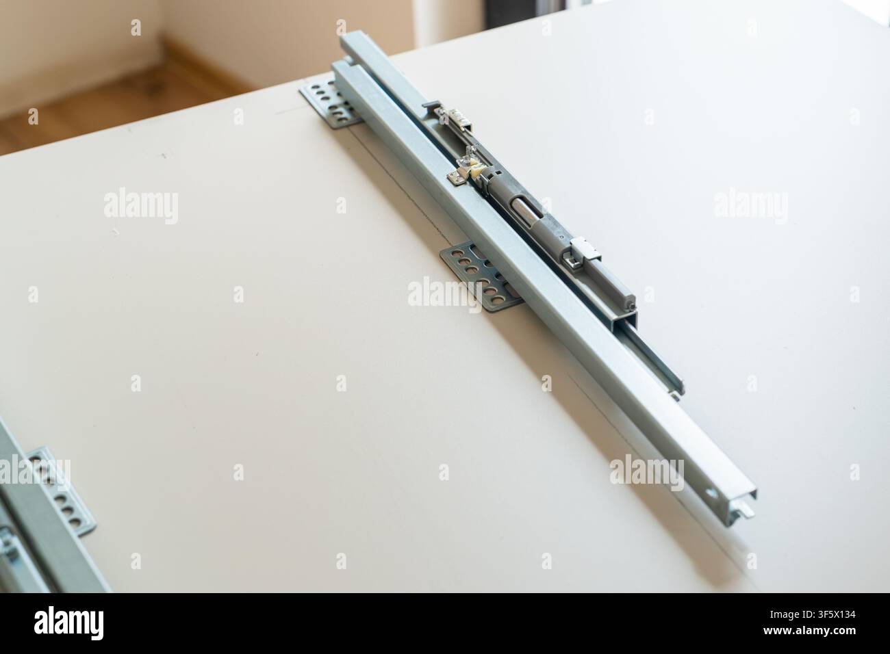 Schiebechanismus, der auf einer glatten Oberfläche für Schrankfunktionalität installiert ist. Die metallische Oberfläche kontrastiert mit der hellen Tischplatte und zeigt klare Linien und modernes Design. Stockfoto