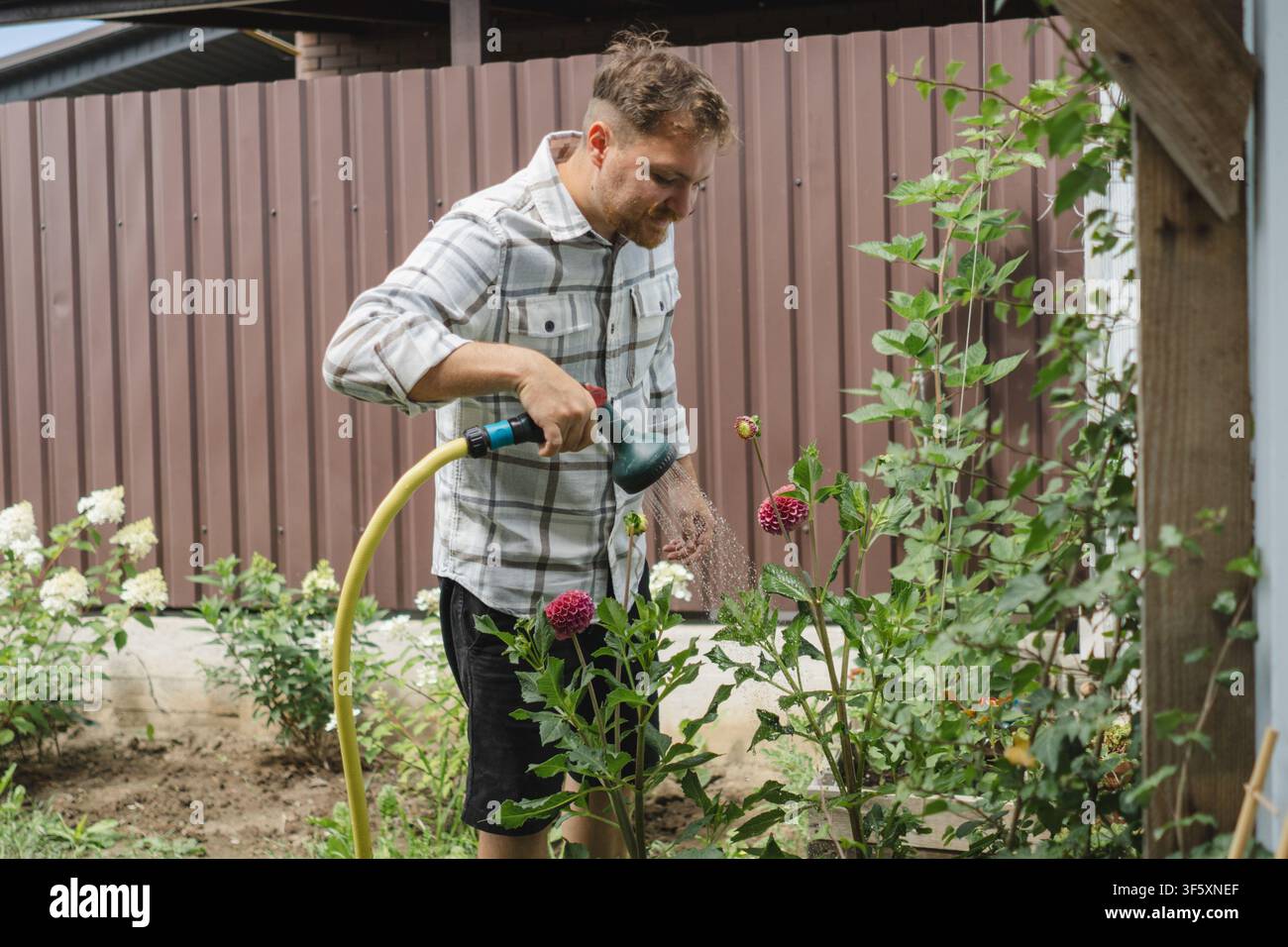Mann gießt Blumen und pflegt einen Hausgarten Stockfoto