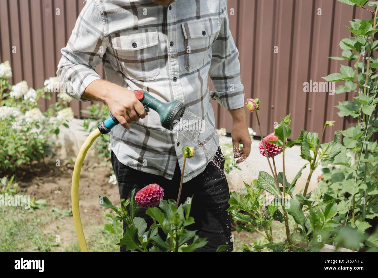 Mann gießt Blumen und pflegt einen Hausgarten Stockfoto
