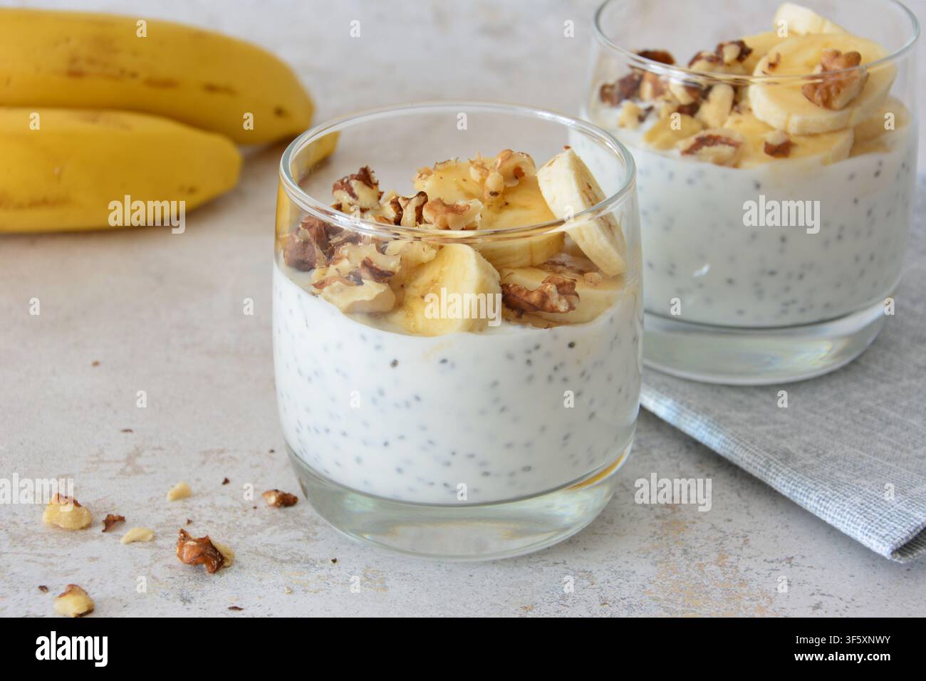 Zwei Gläser Chiasamenpudding mit Bananenscheiben und Walnüssen auf pastellfarbenem Hintergrund Stockfoto