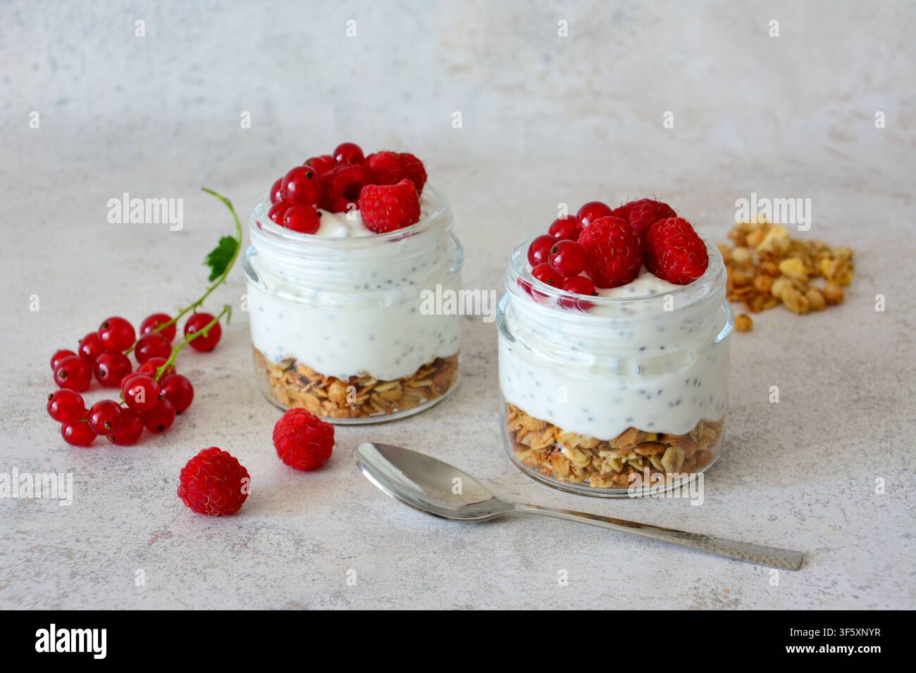 Gesunder Joghurt-Parfait mit Granola und Himbeeren in Glasbehältern, Vorderansicht Stockfoto