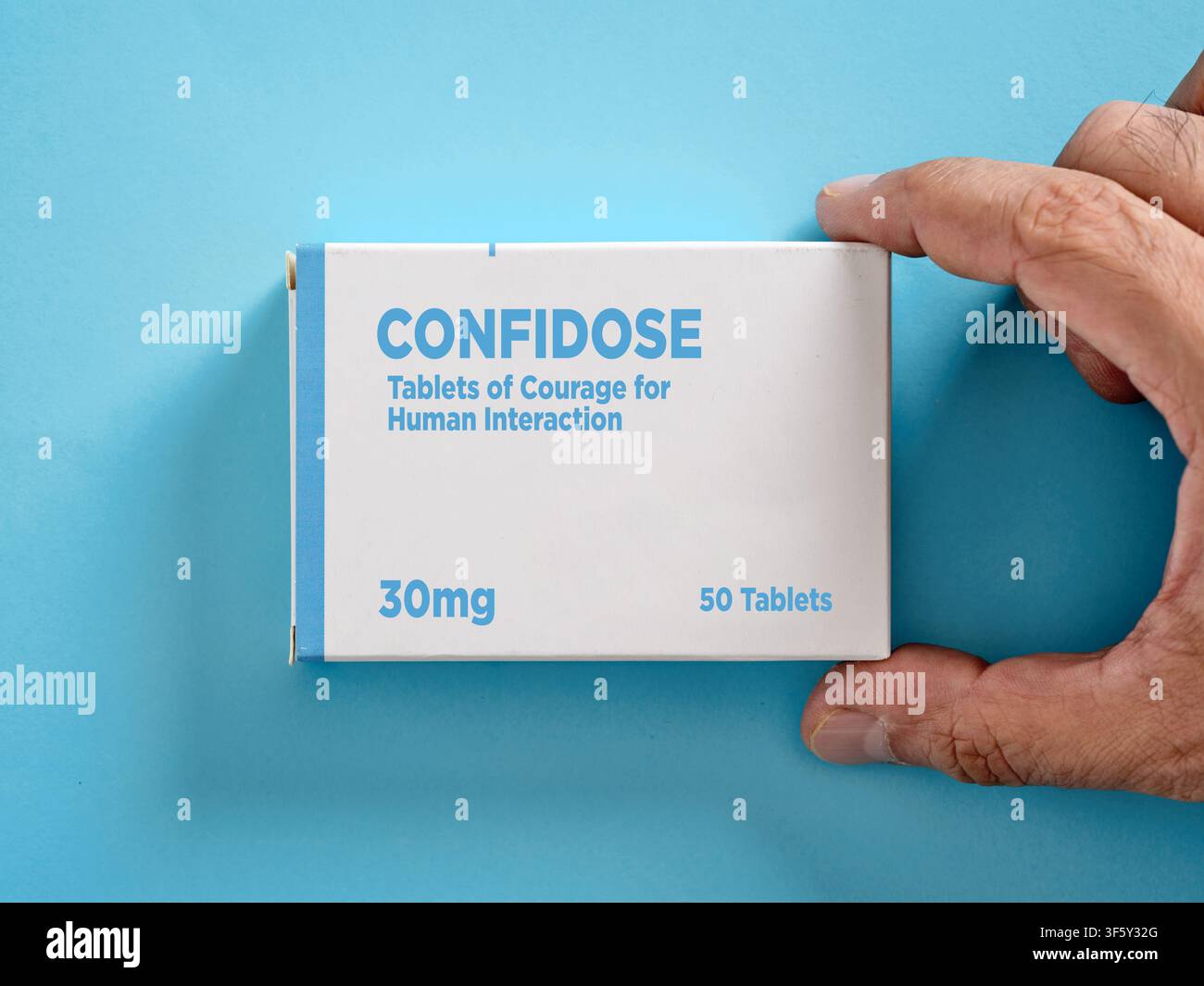 Hand, die eine Schachtel Tabletten hält, die den Mut fördert, um die menschliche Interaktion und das Selbstvertrauen zu stärken, vor einem beruhigenden blauen Hintergrund Stockfoto