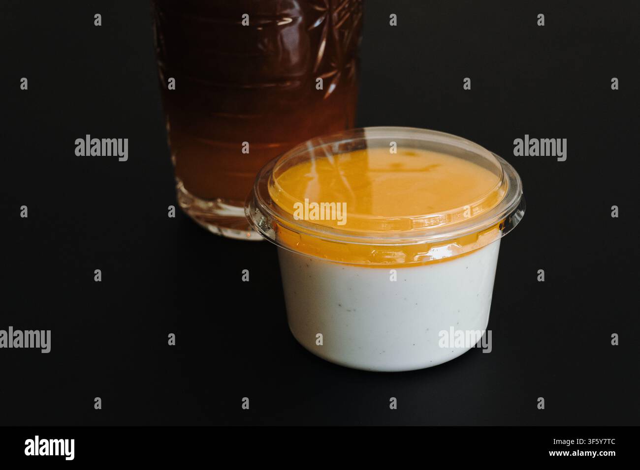 Cremige Vanille-Panna Cotta mit Mangosauce serviert neben einem Glas Eiskaffee. Minimale Café-Präsentation mit Kopierraum auf einem schwarzen Tisch. Stockfoto
