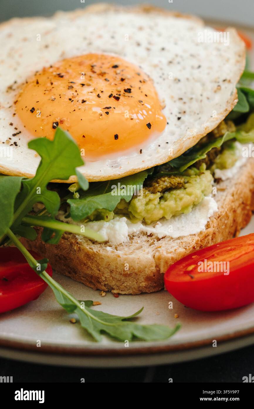 Nahaufnahme von Avocado-Toast, geschichtet mit Avocado, Käse, Rucola und einem Spiegelei. Frisches Gemüse vervollständigt ein nahrhaftes Frühstück. Stockfoto