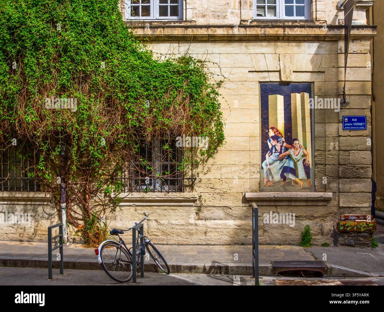 Avignon, Frankreich, 11. April 2026, Fahrrad, das an einem Gebäude mit einem Wandgemälde und einer Kletterpflanze in der Joseph-Vernet-Straße geparkt ist Stockfoto