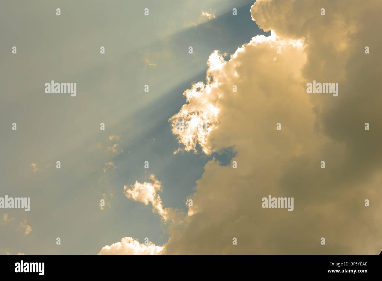 Helles Sonnenlicht strömt durch große goldene Wolken und erzeugt sichtbare Strahlen vor einem blauen Himmel. Stockfoto