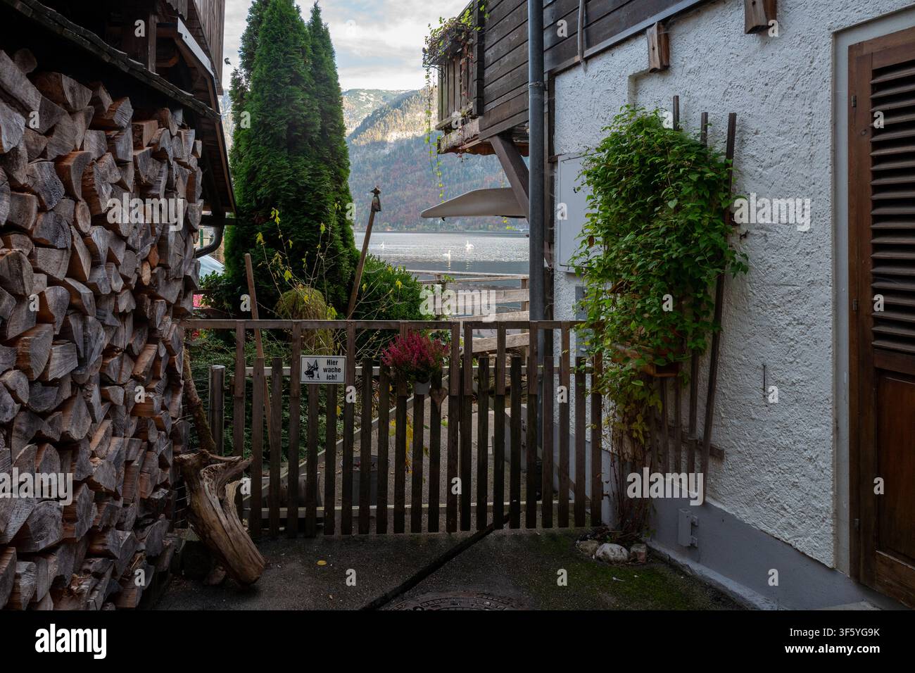 Eine gemütliche Küstenstraße mit einem Holztor, gestapeltem Feuerholz, einem Balkon und Blick auf die Berge am Hallstättersee in Österreich. Stockfoto