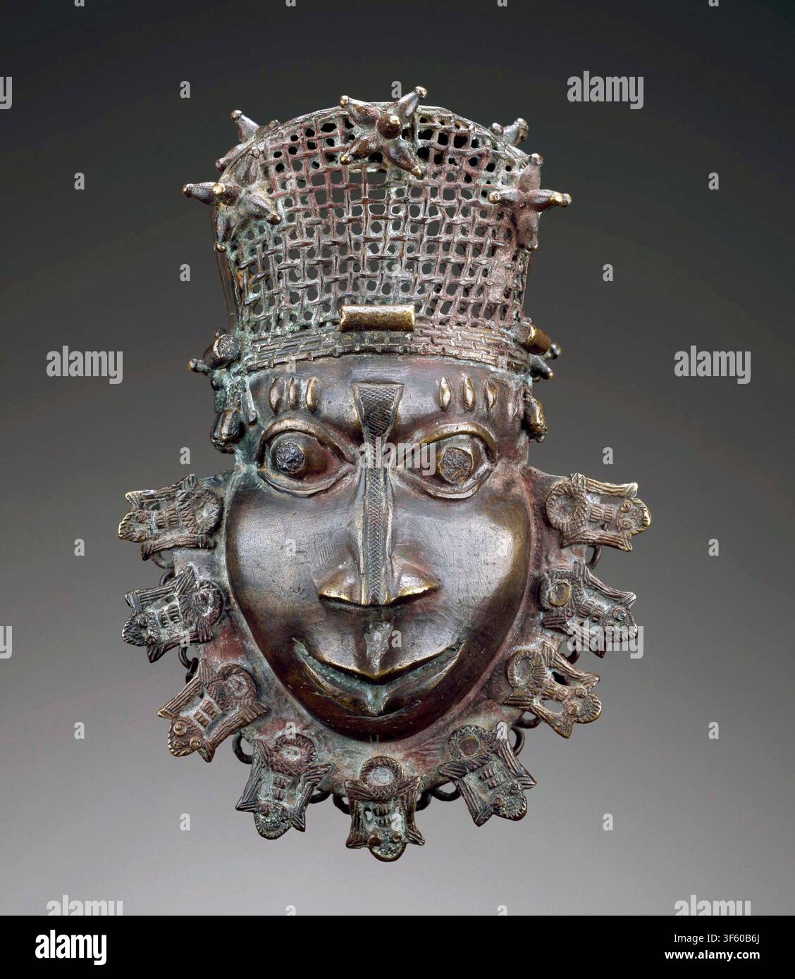 Gusseiser Anhänger in Form eines menschlichen Gesichts aus Kupferlegierung mit durchbrochenem Gitterkopfschmuck, Bart aus neun Schlammfischen und Eisenintarsienaugen. Benin   Datum: 1770er Jahre. Ein historischer königlicher Hüftanhänger aus dem 18. Jahrhundert aus dem historischen Königreich Benin (heute Nigeria), gefertigt von der erblichen königlichen Gießergilde (Ìgùn Ẹ́rọ̀nwwọ̀n). Stockfoto