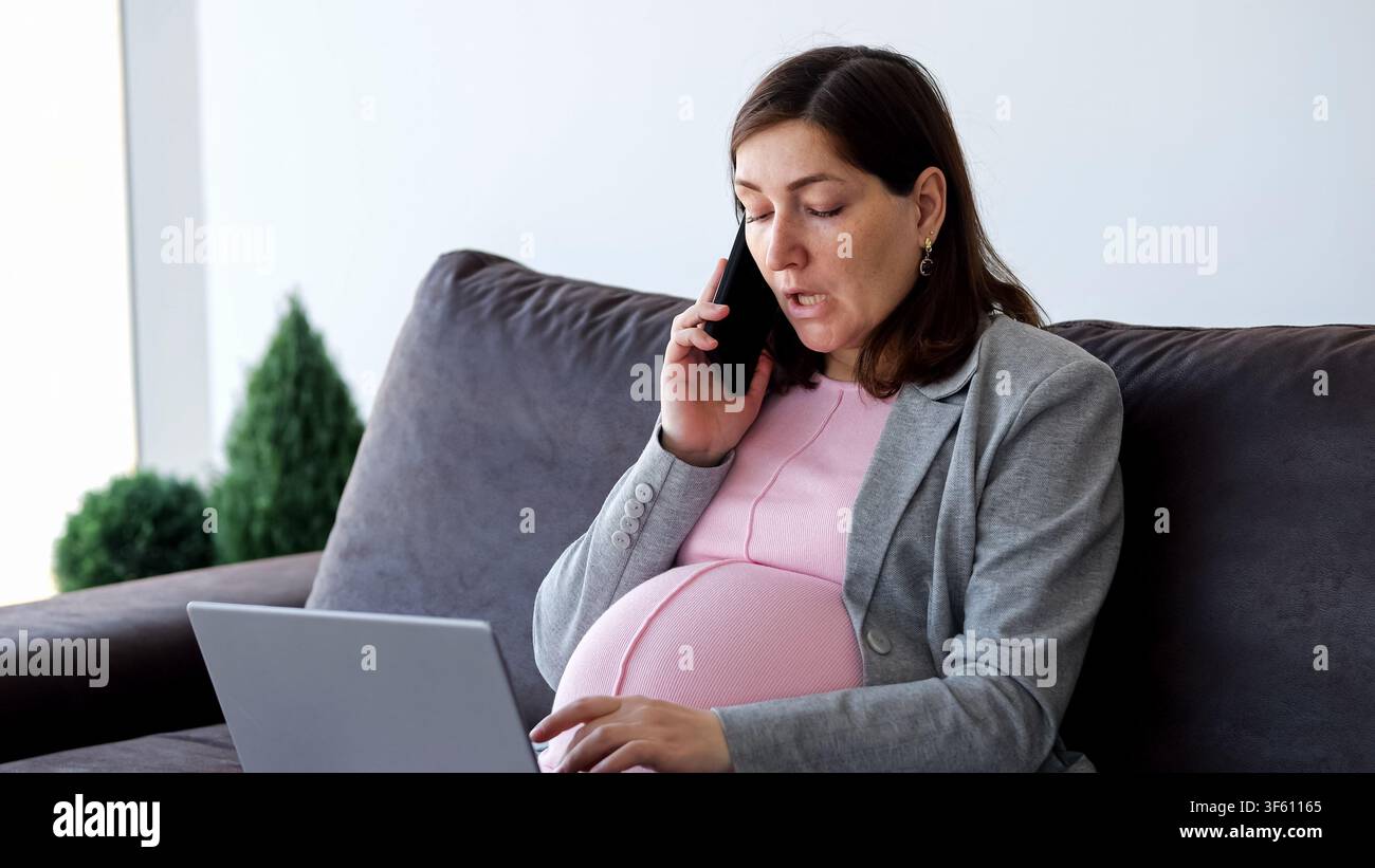 Schwangere Frau arbeitet von zu Hause aus mit Laptop und Telefon Stockfoto