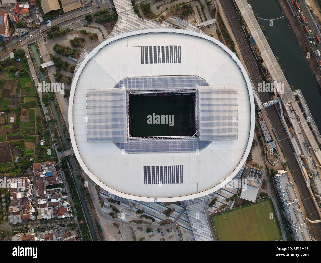 Luftbild des Jakarta International Stadium mit seinem markanten Schiebedach und dem grünen Spielfeld, umgeben von urbaner Infrastruktur und Grünflächen Stockfoto
