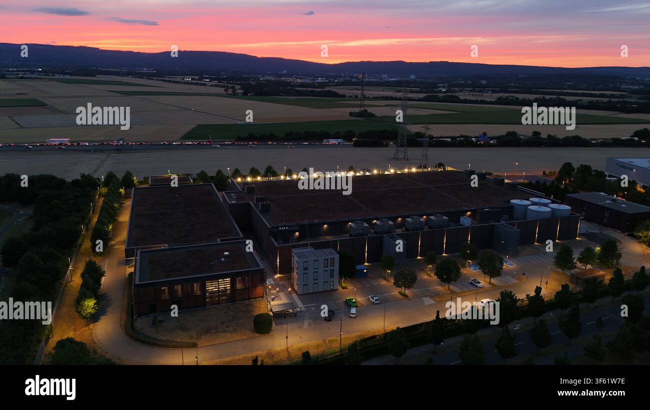 Luftbild der Iron Mountain Data Centers FRA-2 bei Dämmerung beleuchtet mit einem lebendigen Sonnenuntergangshimmel über den umliegenden Feldern und Straßen in Frankfurt am Main Stockfoto